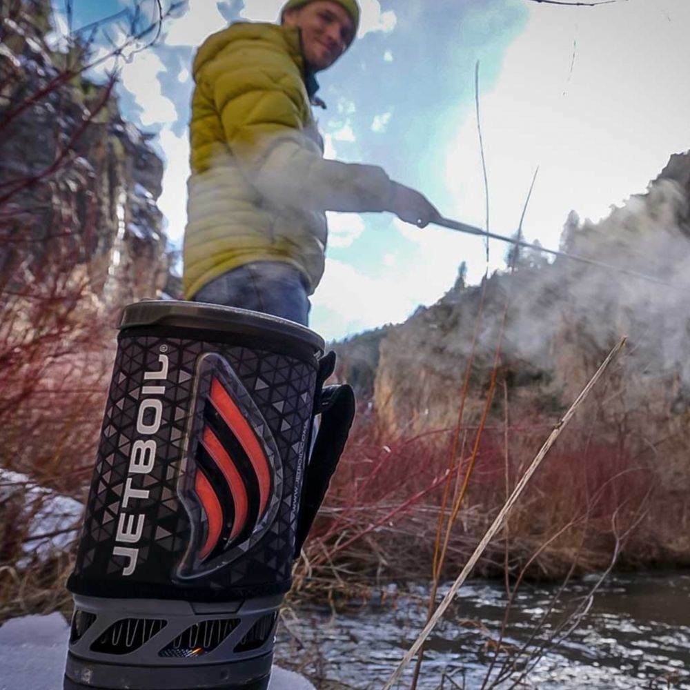 Person using a Jetboil stove outdoors with a snowy landscape in the background