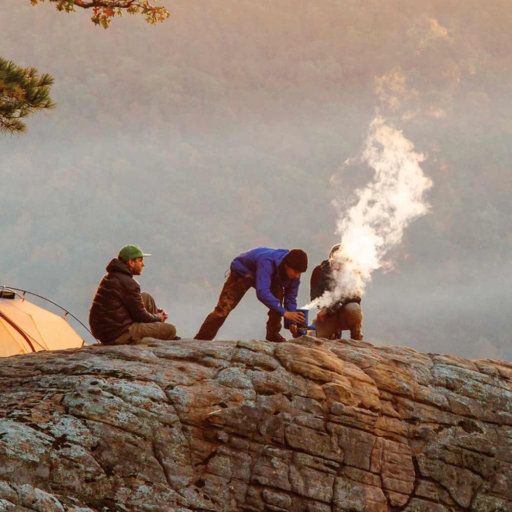 Two people camping on a rocky outcrop with a tent and cooking equipment.