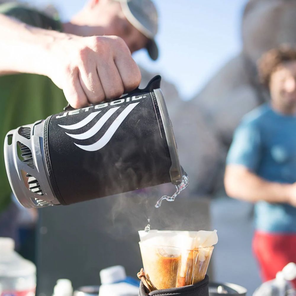 Person pouring coffee from a portable coffee maker into a cup outdoors.