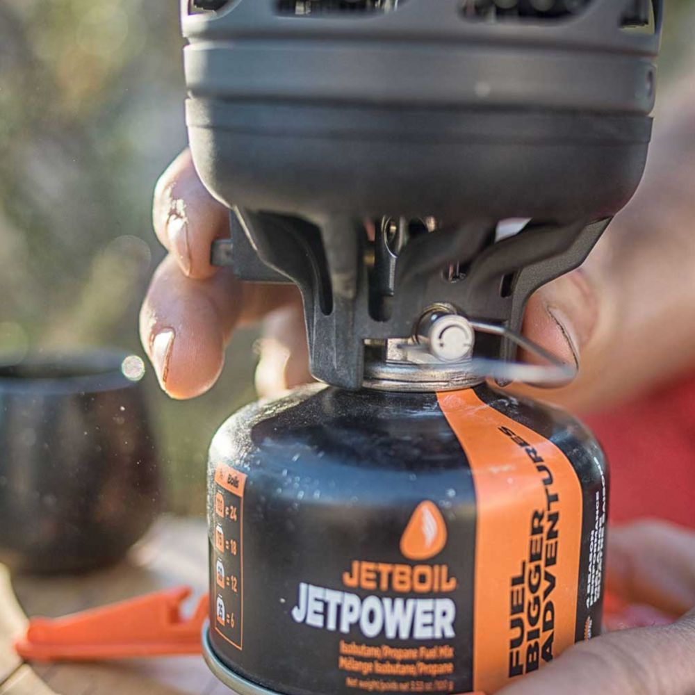 Person holding a Jetboil fuel canister with a blurred outdoor background