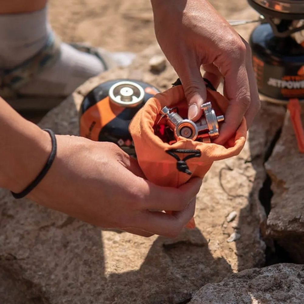 Person holding a small orange container with camping gear on a rocky surface