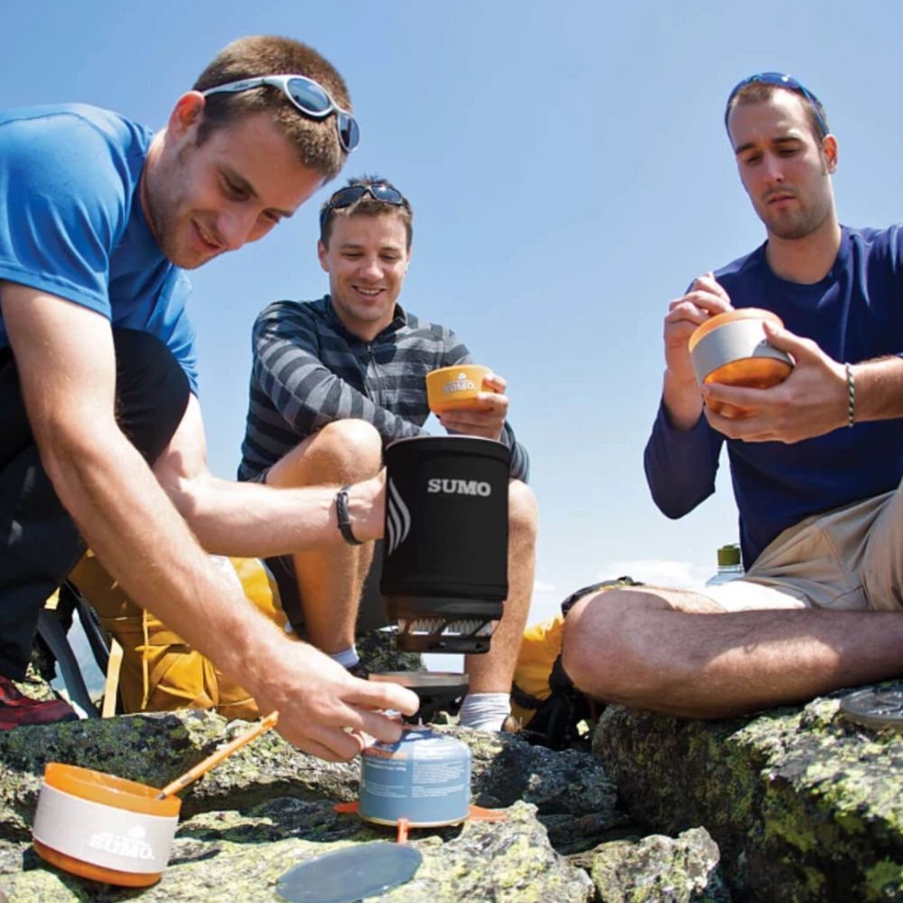 Three men outdoors using SUMO brand cookware on a sunny day.