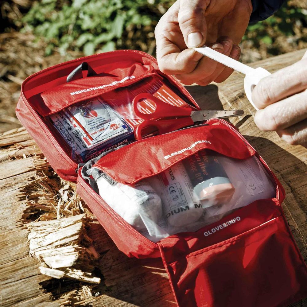 Lifesystems Explorer First Aid Kit open on a wooden surface with hands interacting with its contents.