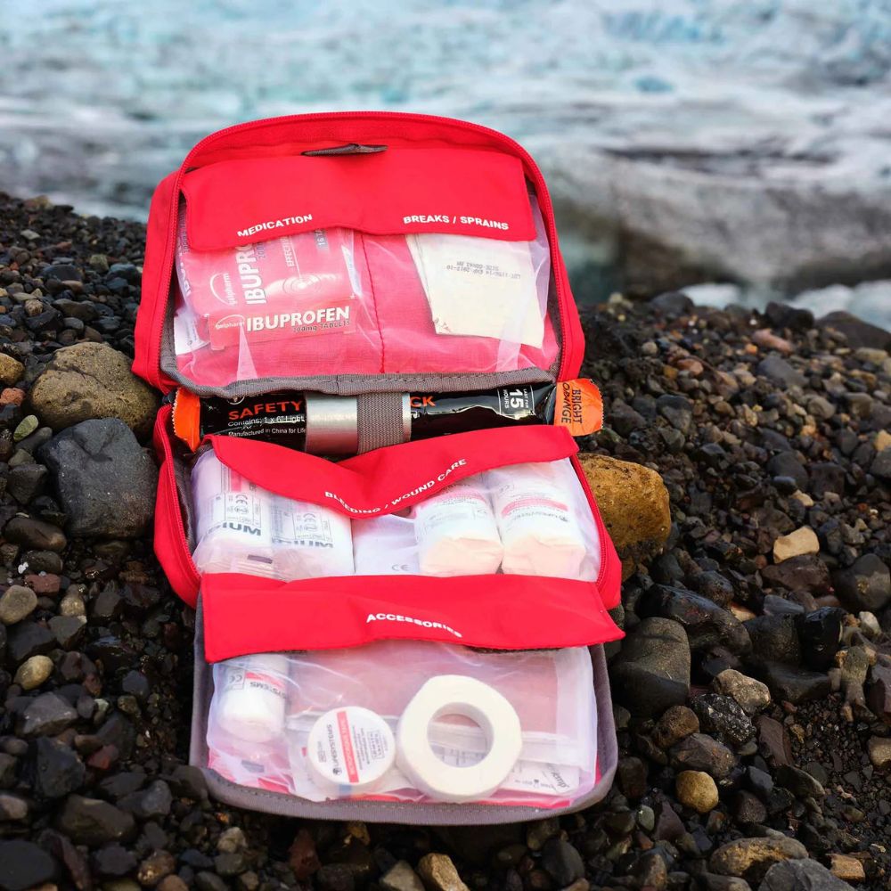 Lifesystems Mountain First Aid Kit open on a rocky surface with a blurred natural background
