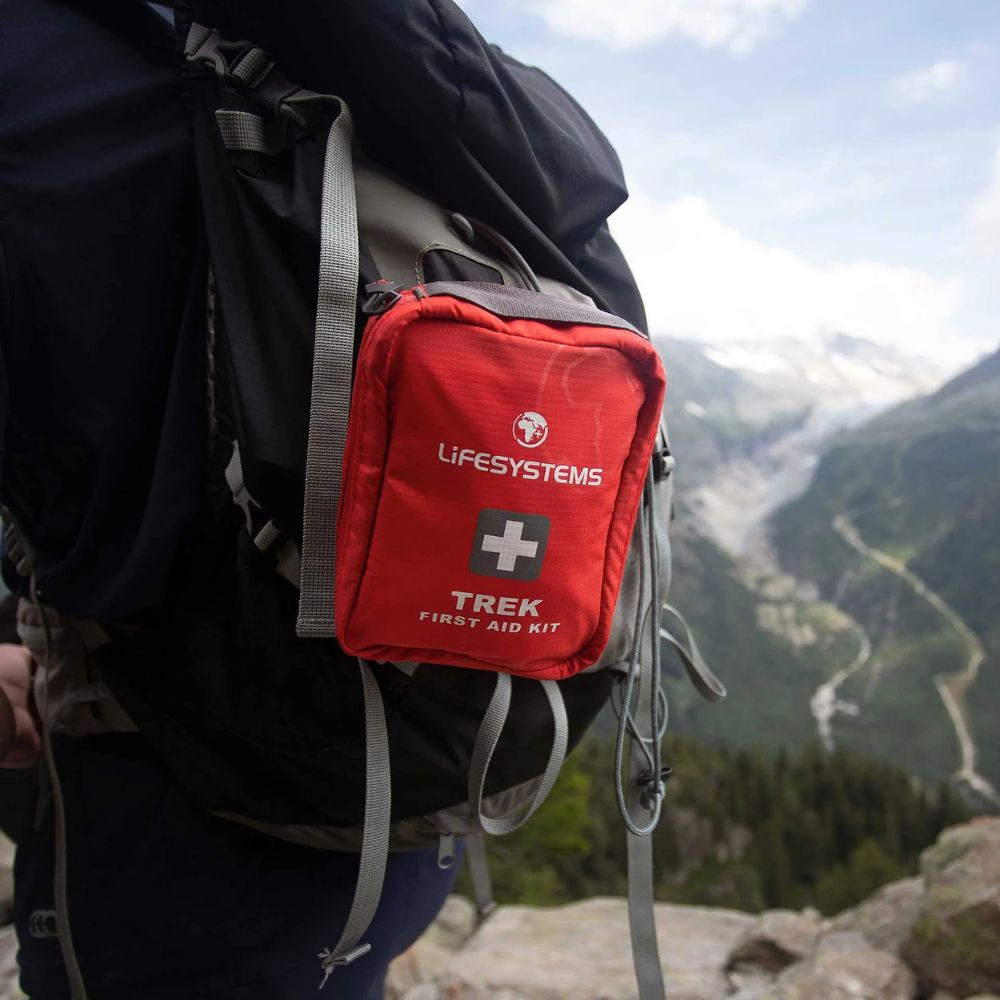 Red Lifesystems Trek First Aid Kit attached to a backpack with a mountainous landscape in the background
