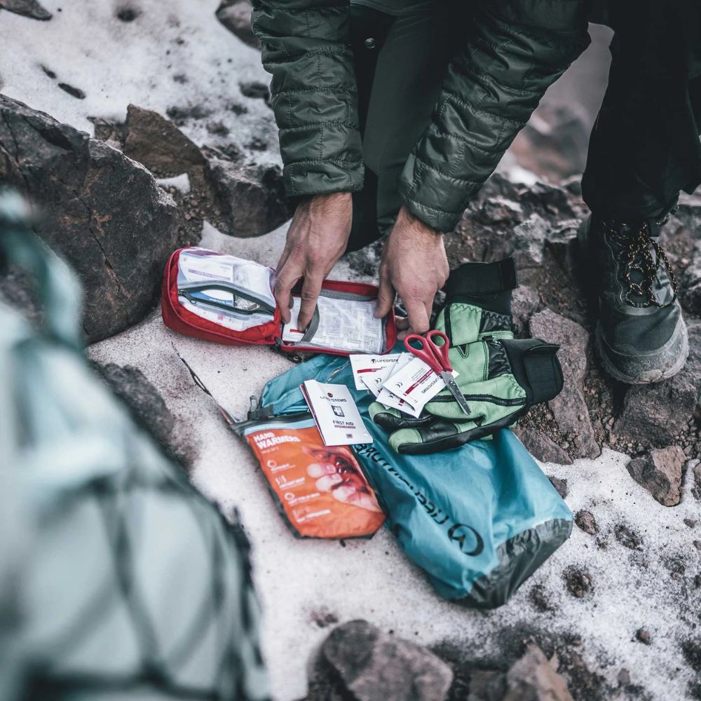 Person organizing medical supplies in a backpack on a snowy ground