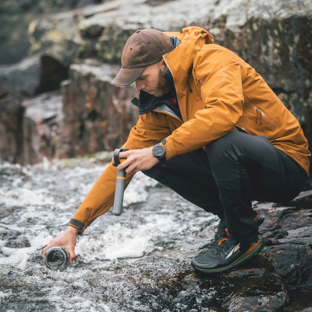 Person in a yellow jacket filtering water from a stream in a natural setting