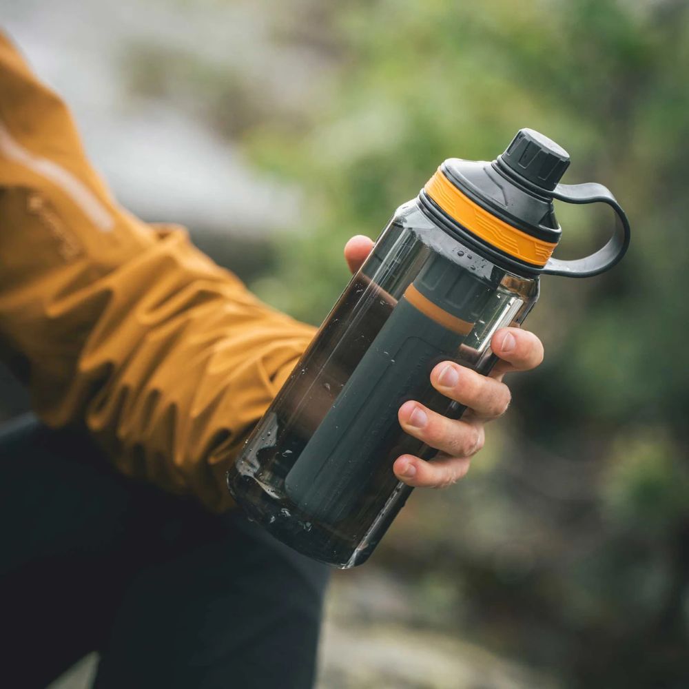 Person holding a black and yellow insulated bottle with a blurred natural background
