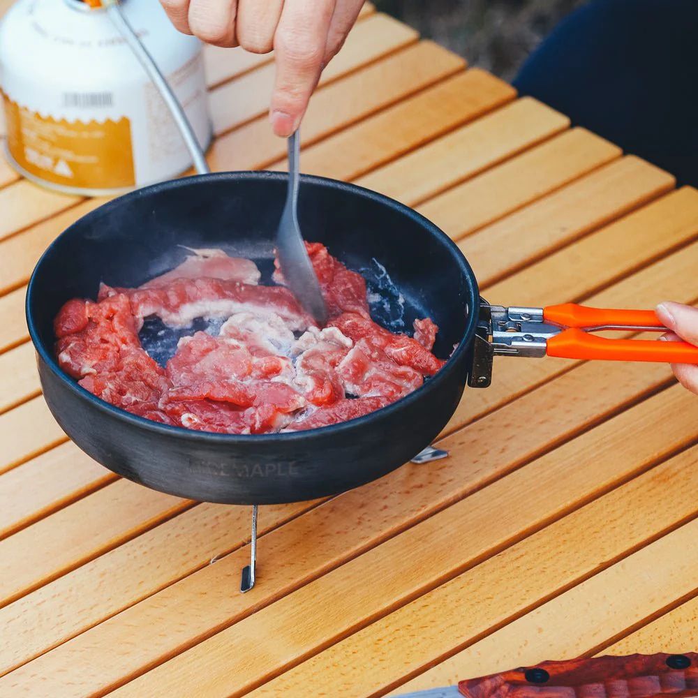 Person cooking ground meat in a portable frying pan on a wooden surface