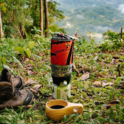 Cup of coffee on a grassy hillside with hiking boots and a thermos in the background