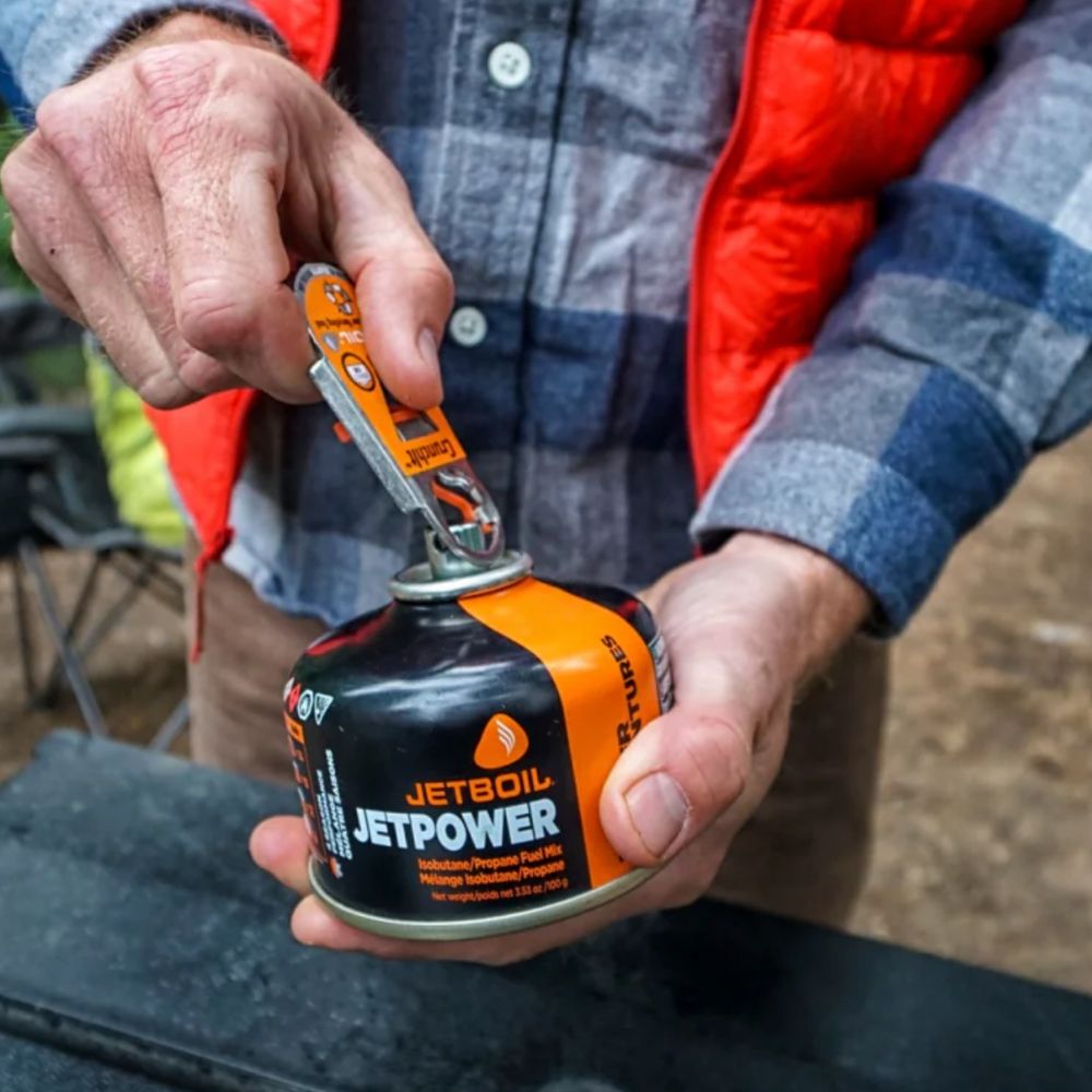 Person using a Jetboil fuel canister with a multi-tool outdoors.