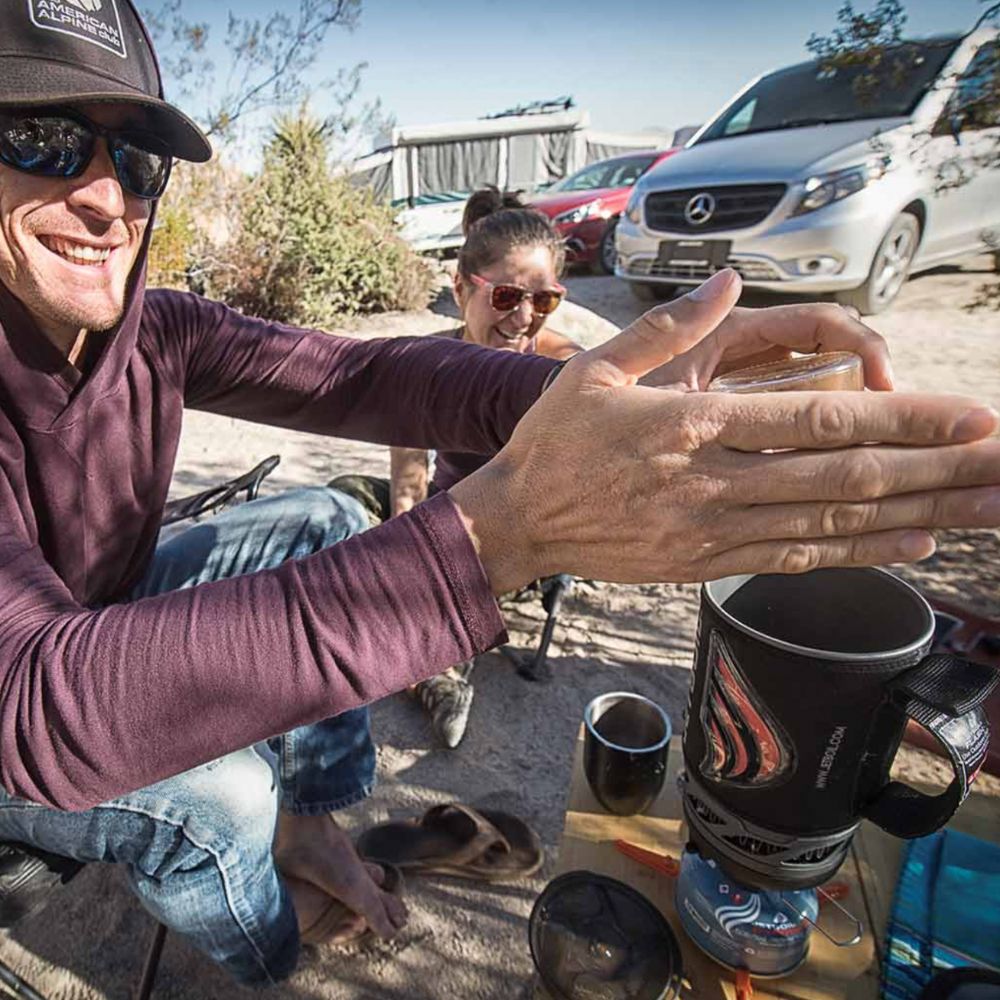 Person outdoors with coffee mugs and a vehicle in the background