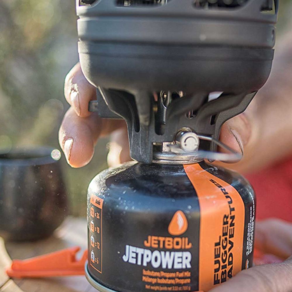 Person holding a Jetboil fuel canister with a blurred outdoor background