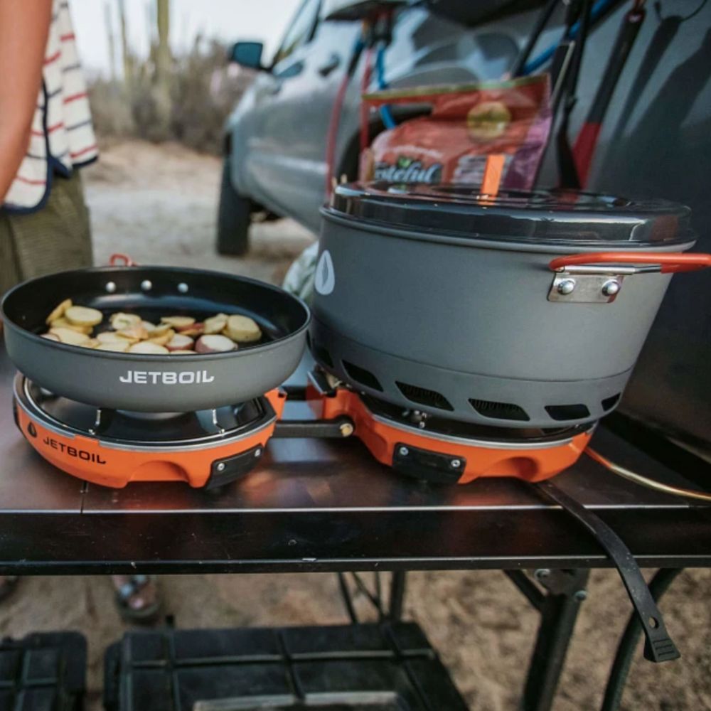 Jetboil camping stove with food cooking on a table outdoors.