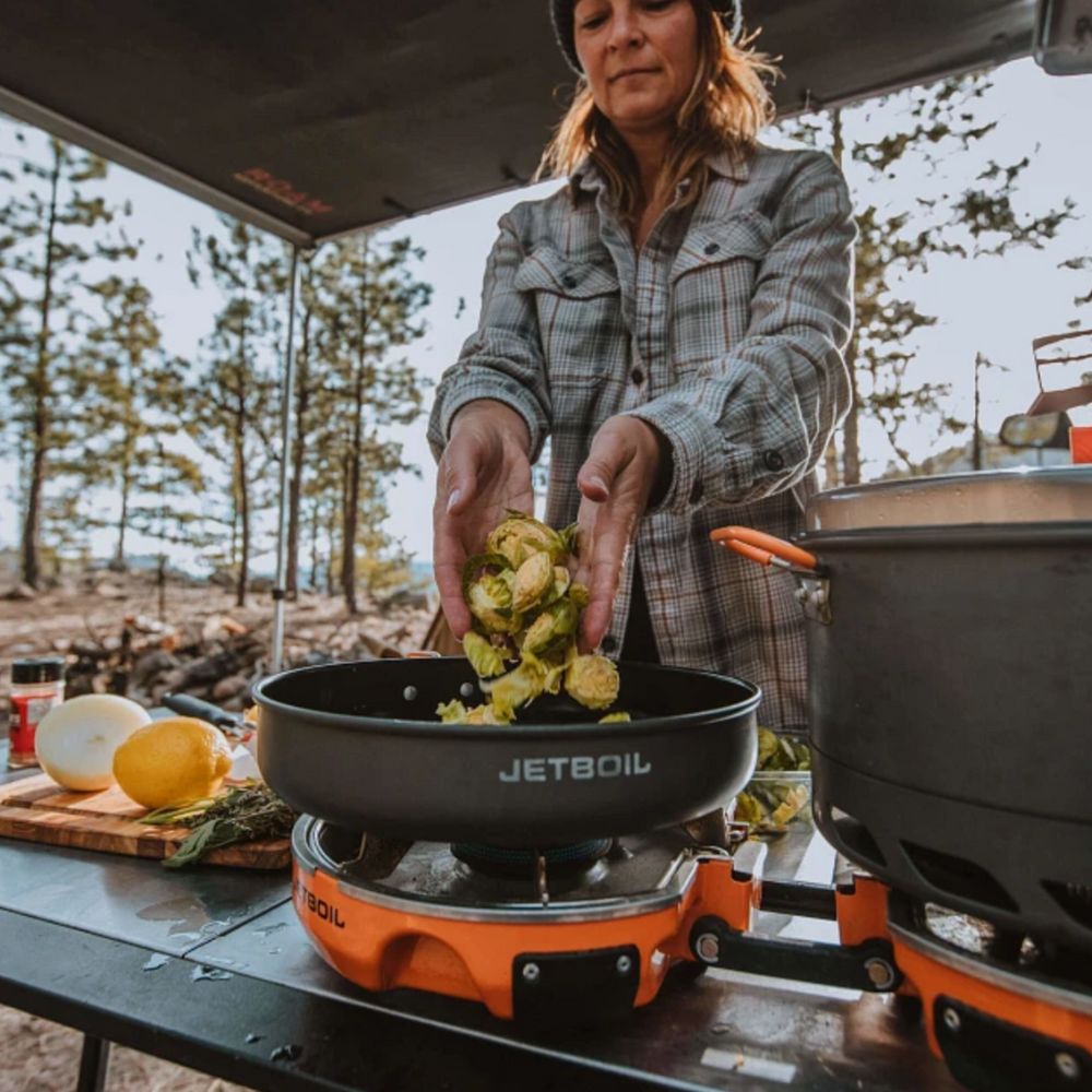 Person cooking outdoors using a Jetboil stove in a forest setting