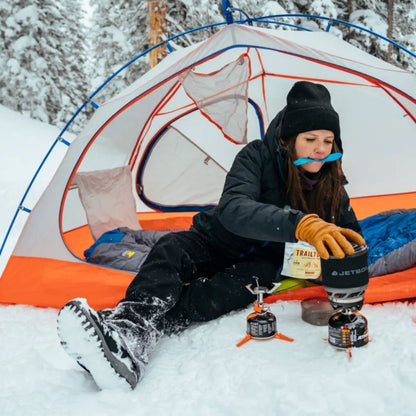 Person camping in the snow with a tent and camping stove.