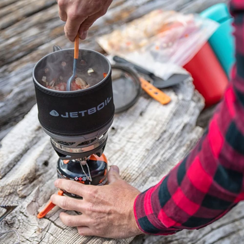 Person using a Jetboil cooking system outdoors on a wooden surface.