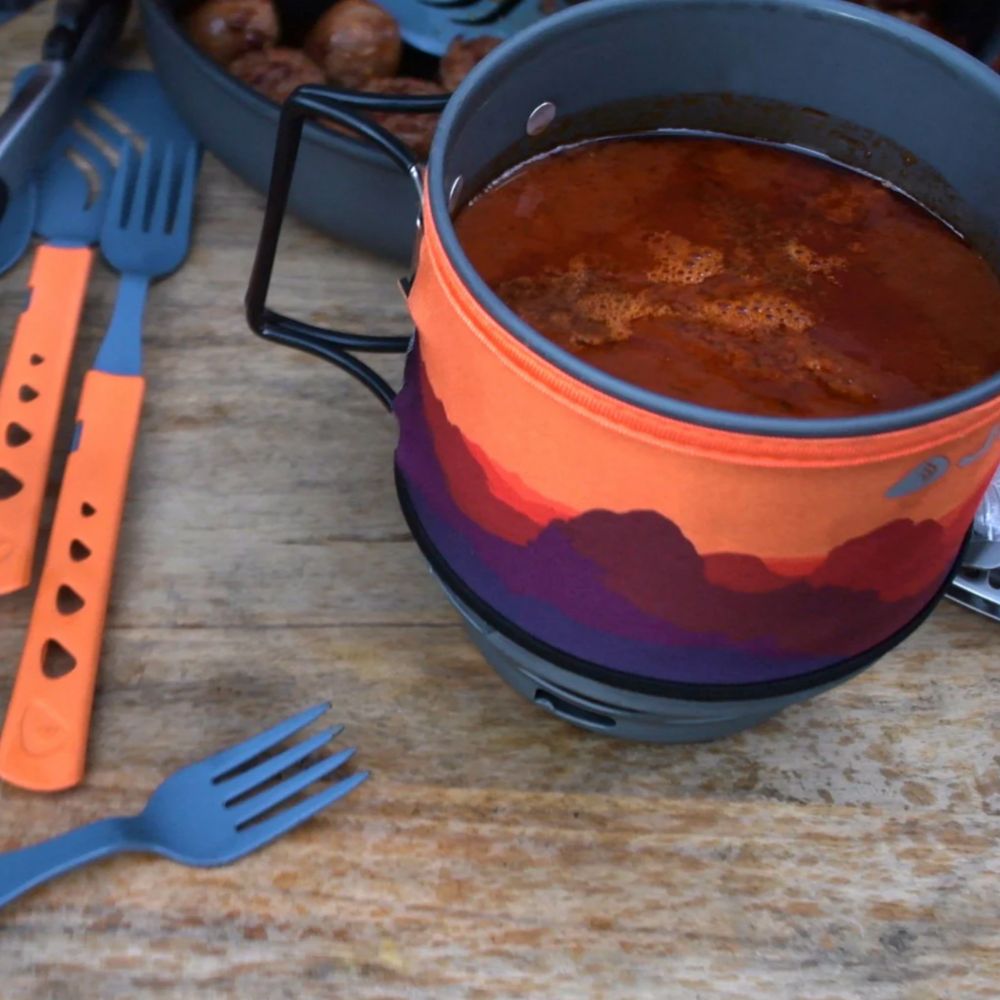 Camping pot with colorful design on a wooden surface with utensils.
