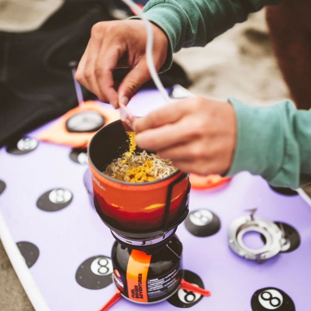 Person preparing food on a camping stove with a focus on the hands and cooking process.