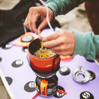 Person preparing food on a camping stove with a focus on the hands and cooking process.