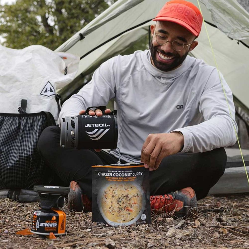 Man preparing a meal outdoors with a Jetboil stove and food package.