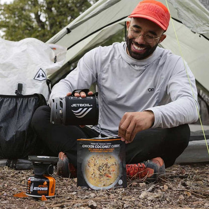 Man preparing a meal outdoors with a Jetboil stove and food package.