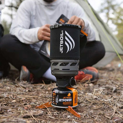 Jetboil stove system on the ground with a person sitting in the background.