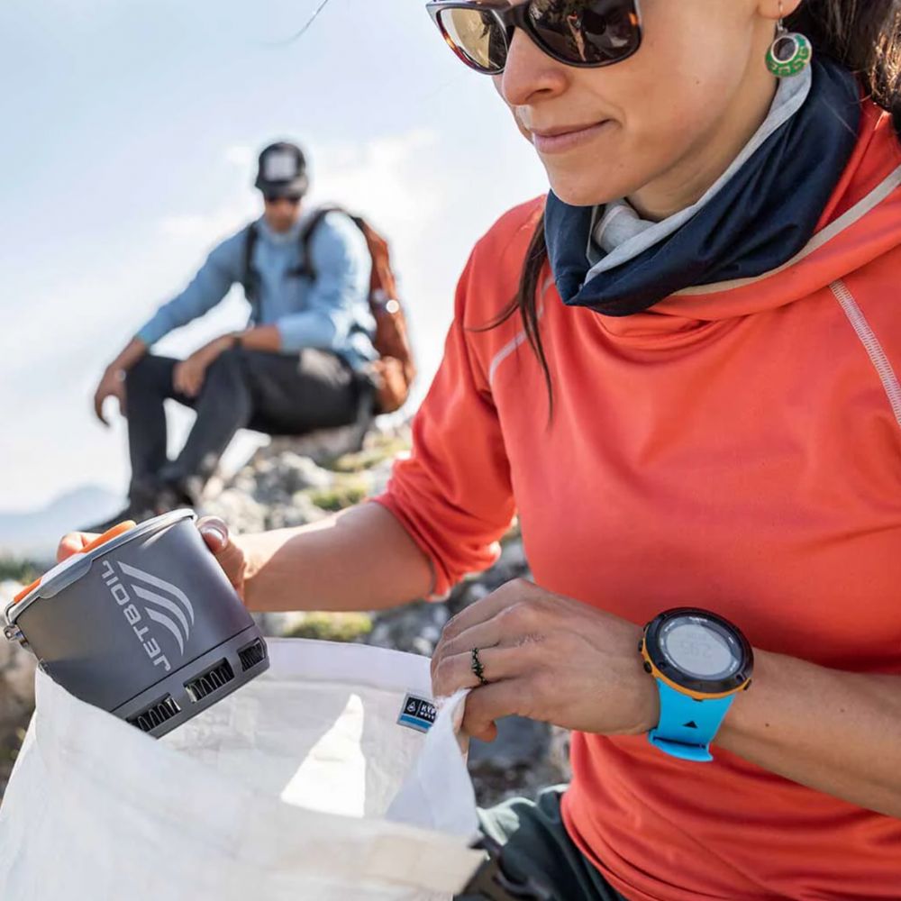 Person in outdoor setting with a Jetboil stove and watch, another person in the background.