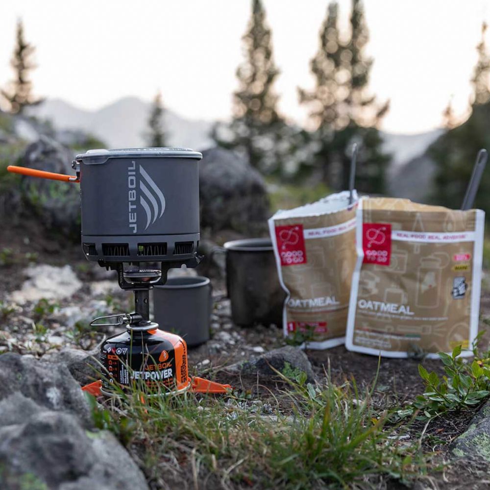 Camping stove with fuel canister and oatmeal packets in a natural setting