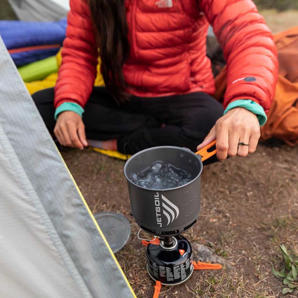 Person camping with a Jetboil stove and pot on a grassy area
