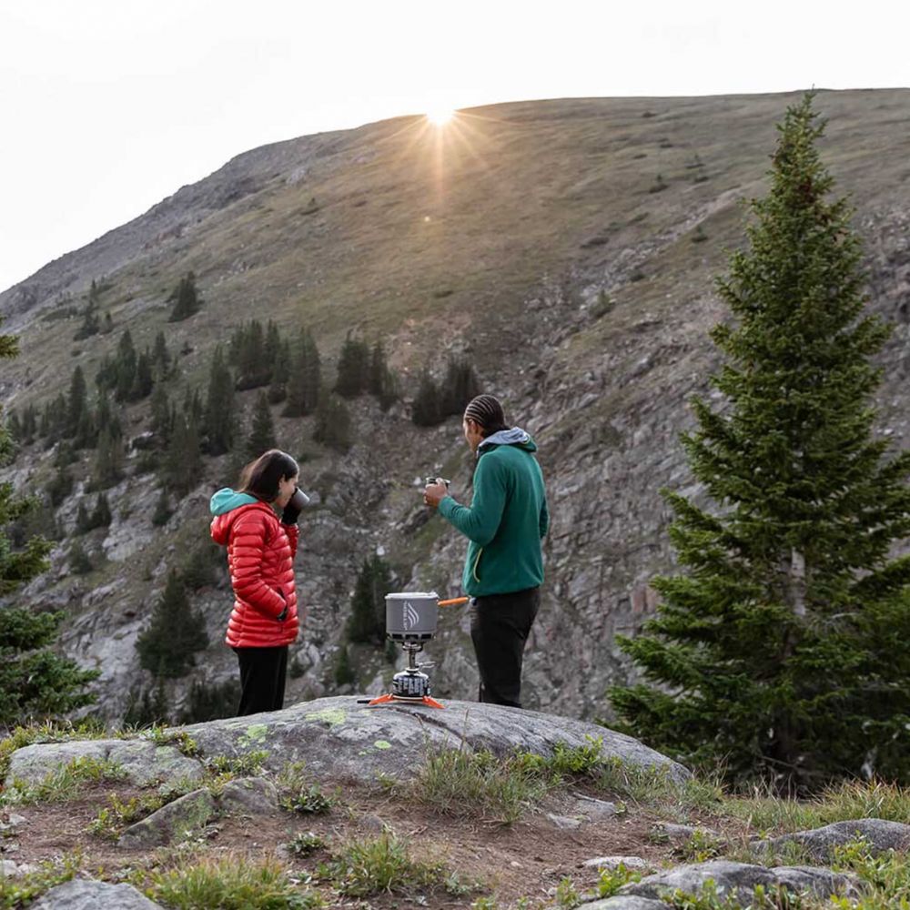 Two people cooking outdoors on a mountain with a portable stove.