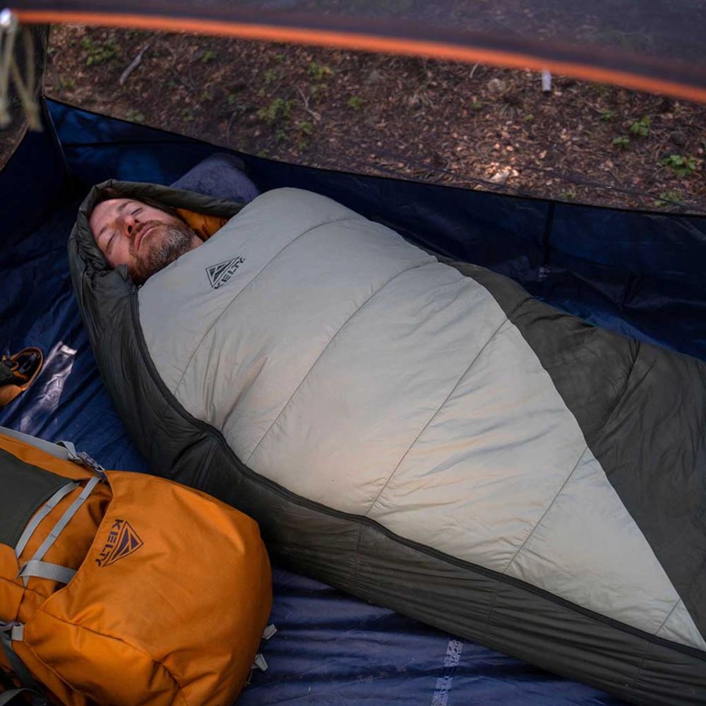 Person sleeping in a sleeping bag inside a tent with an orange backpack nearby.