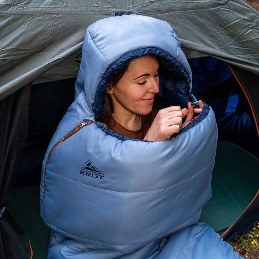Person wearing a blue Kelty sleeping bag inside a tent