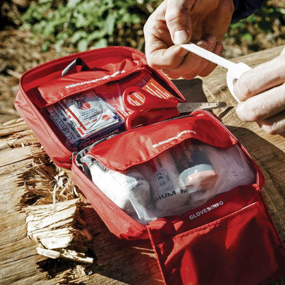 Lifesystems Explorer First Aid Kit open on a wooden surface with hands interacting with its contents.