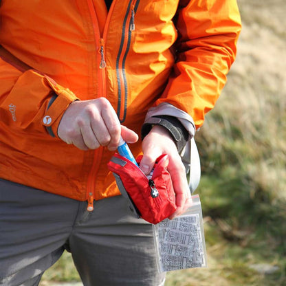Person in orange jacket using Lifesystems Pocket First Aid Kit outdoors. 