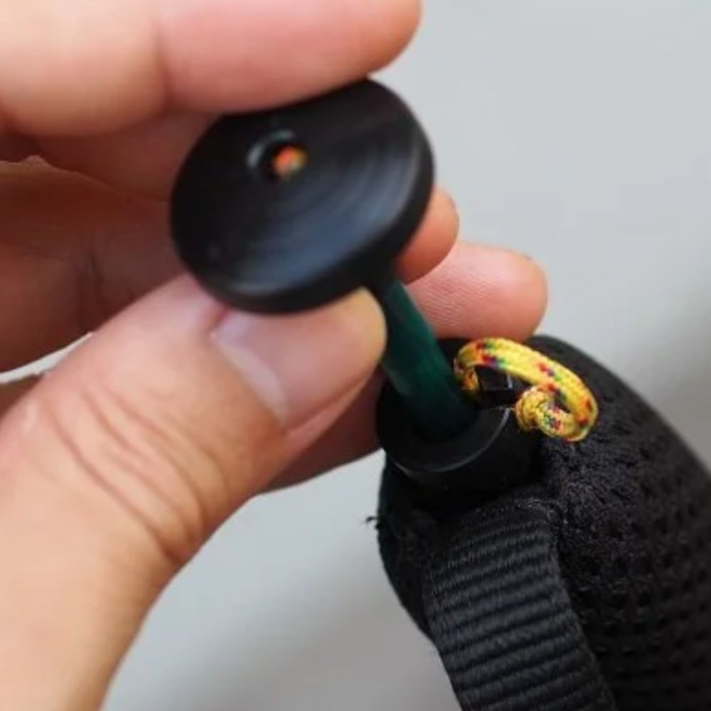 Hand holding a black button with a green string attached, against a neutral background