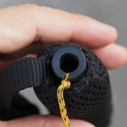 Black textured object with a colorful string held by a hand against a gray background