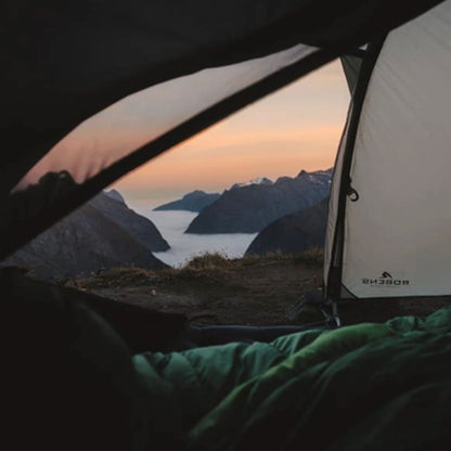 Camping scene with a tent overlooking a mountainous landscape during sunset.